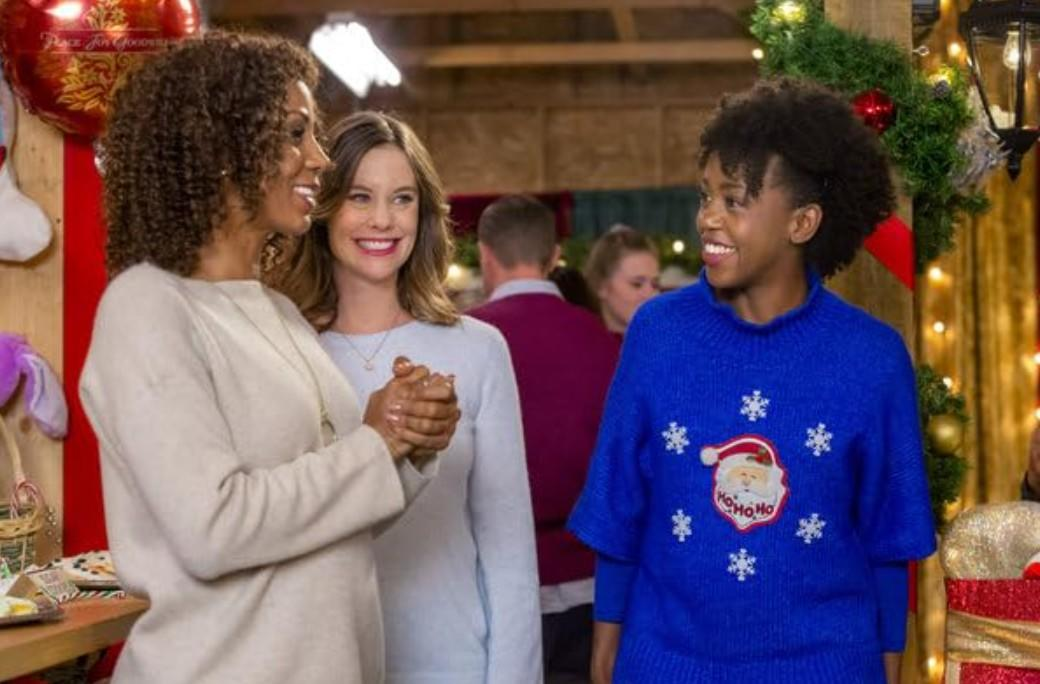 Drei Frauen lachen in weihnachtlicher Deko. Eine trägt einen Pullover mit Weihnachtsmann.