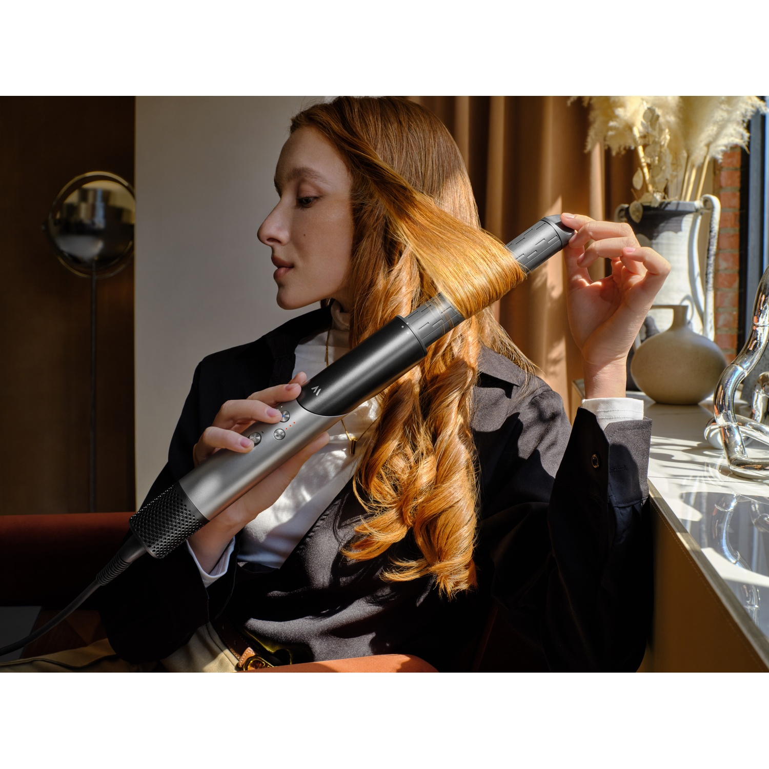 Une femme aux cheveux roux utilise un fer à friser dans une pièce lumineuse.