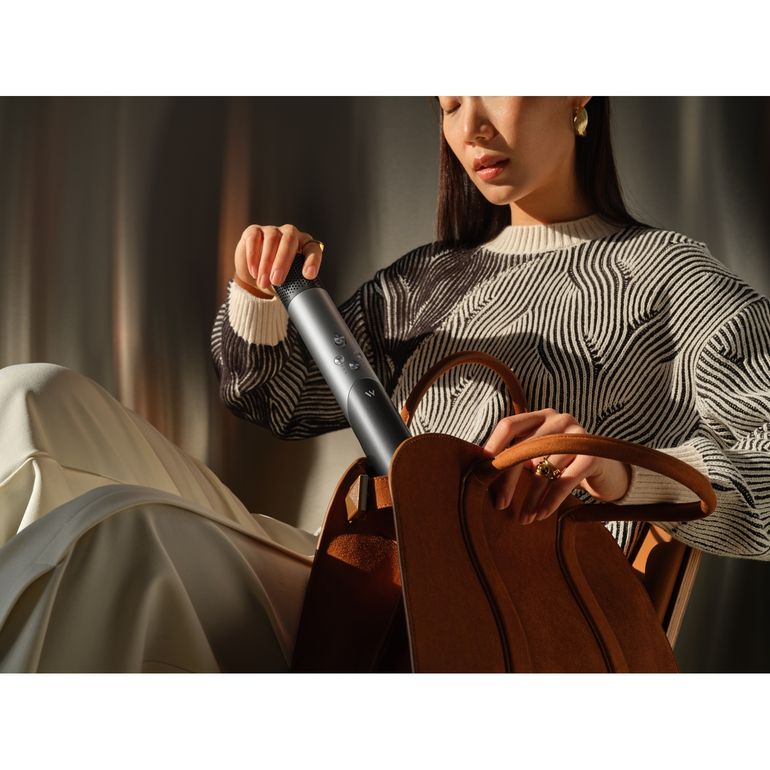 Femme en pull rayé plaçant un cylindre gris dans un sac marron. Fond neutre.