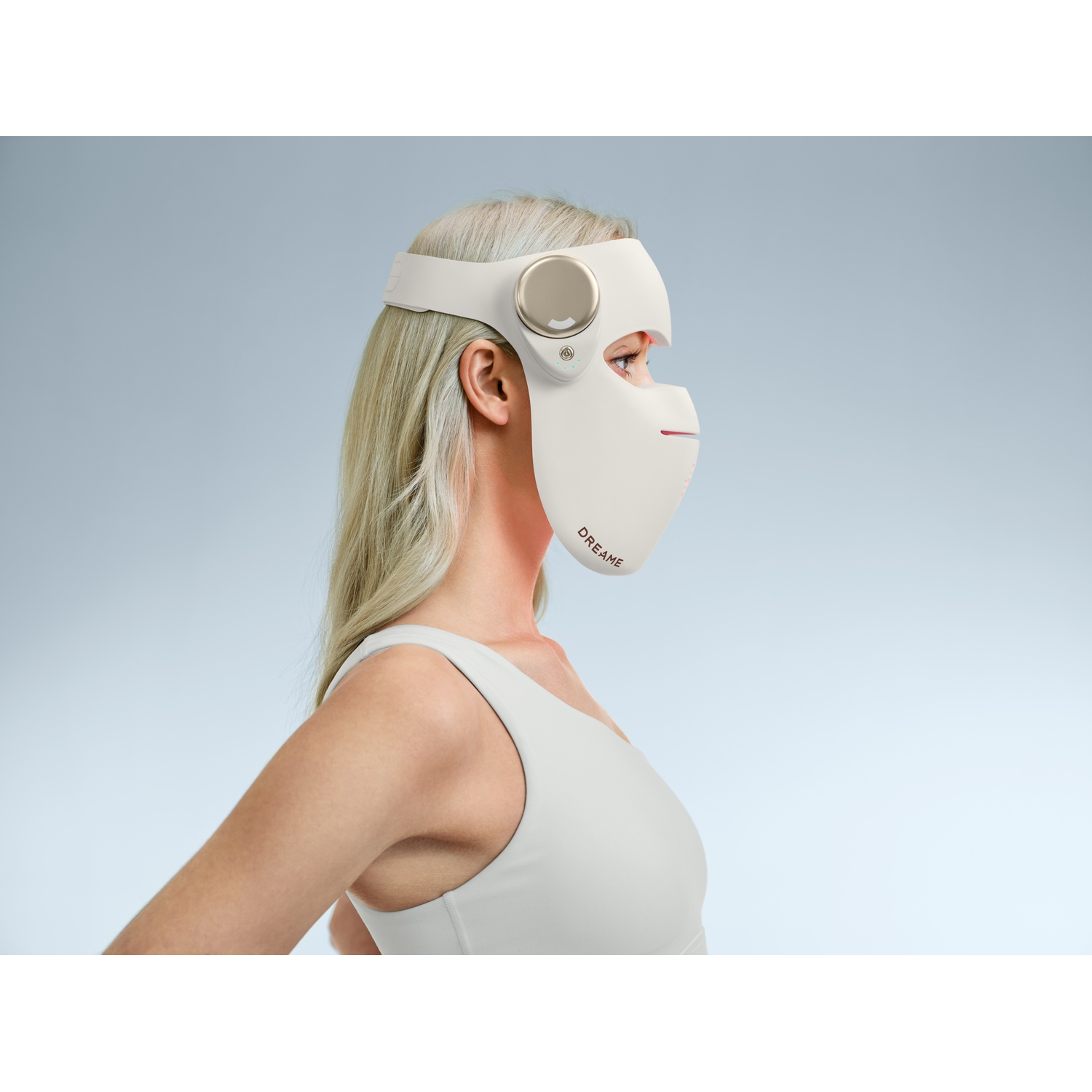 Femme portant un masque facial LED blanc avec logo 'DREAME', cheveux blonds clairs, haut gris.