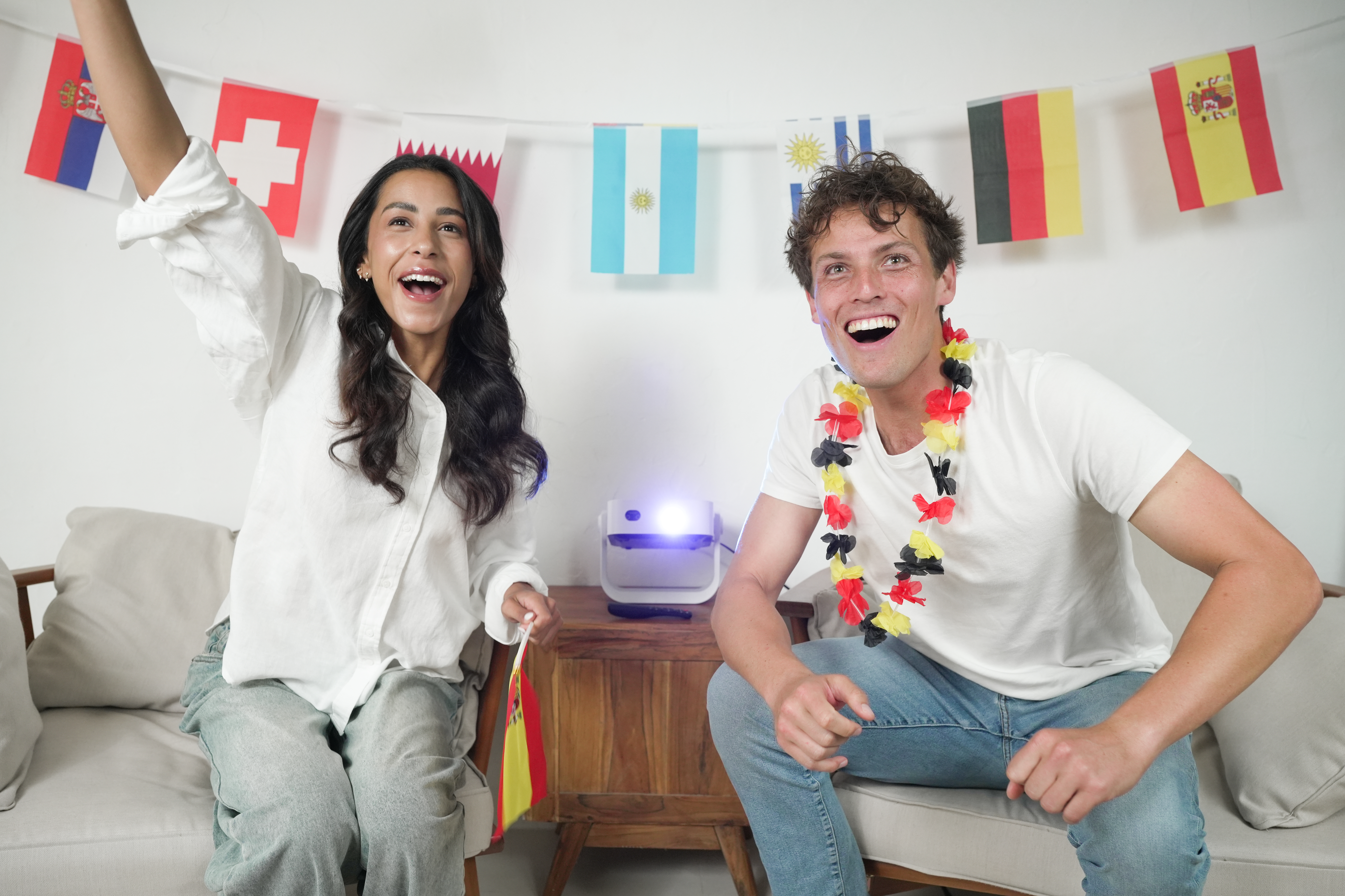 Zwei Menschen jubeln vor Flaggen und einem Projektor.