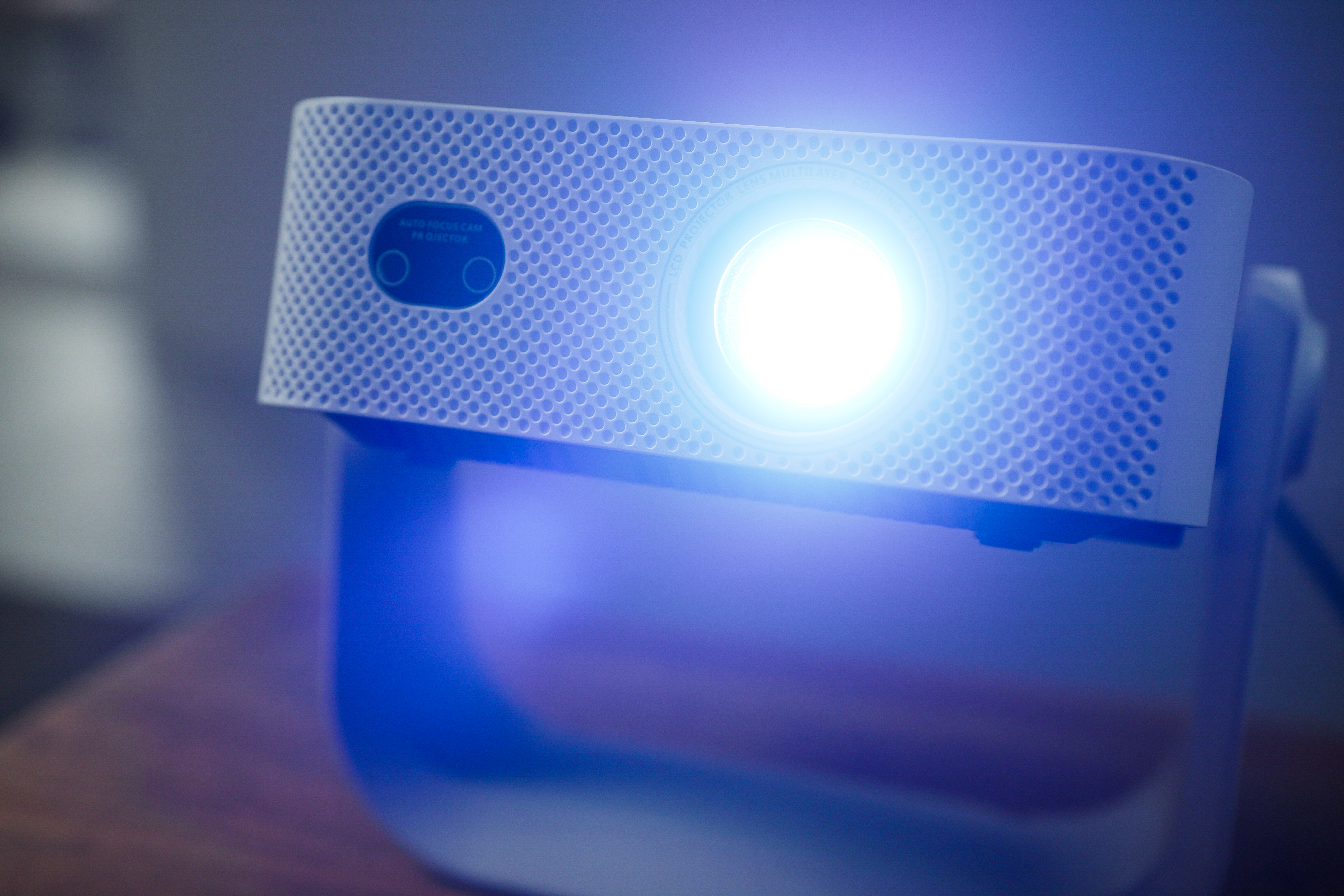 Ein weißer Projektor leuchtet hellblau auf einem Tisch. Der Fokus ist auf dem Objekt.