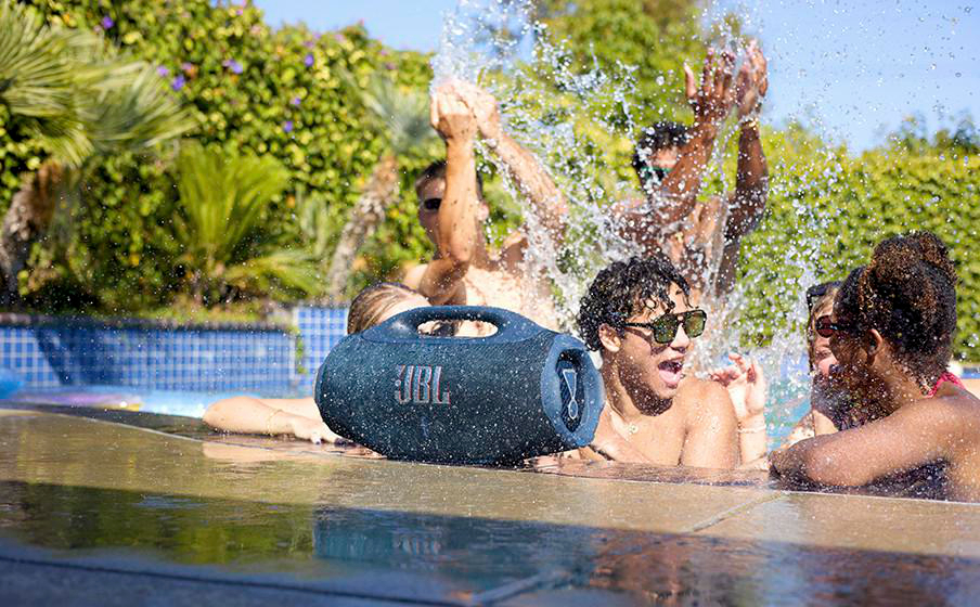 Leute planschen im Pool mit JBL-Lautsprecher, Wasserspritzer im Freien.
