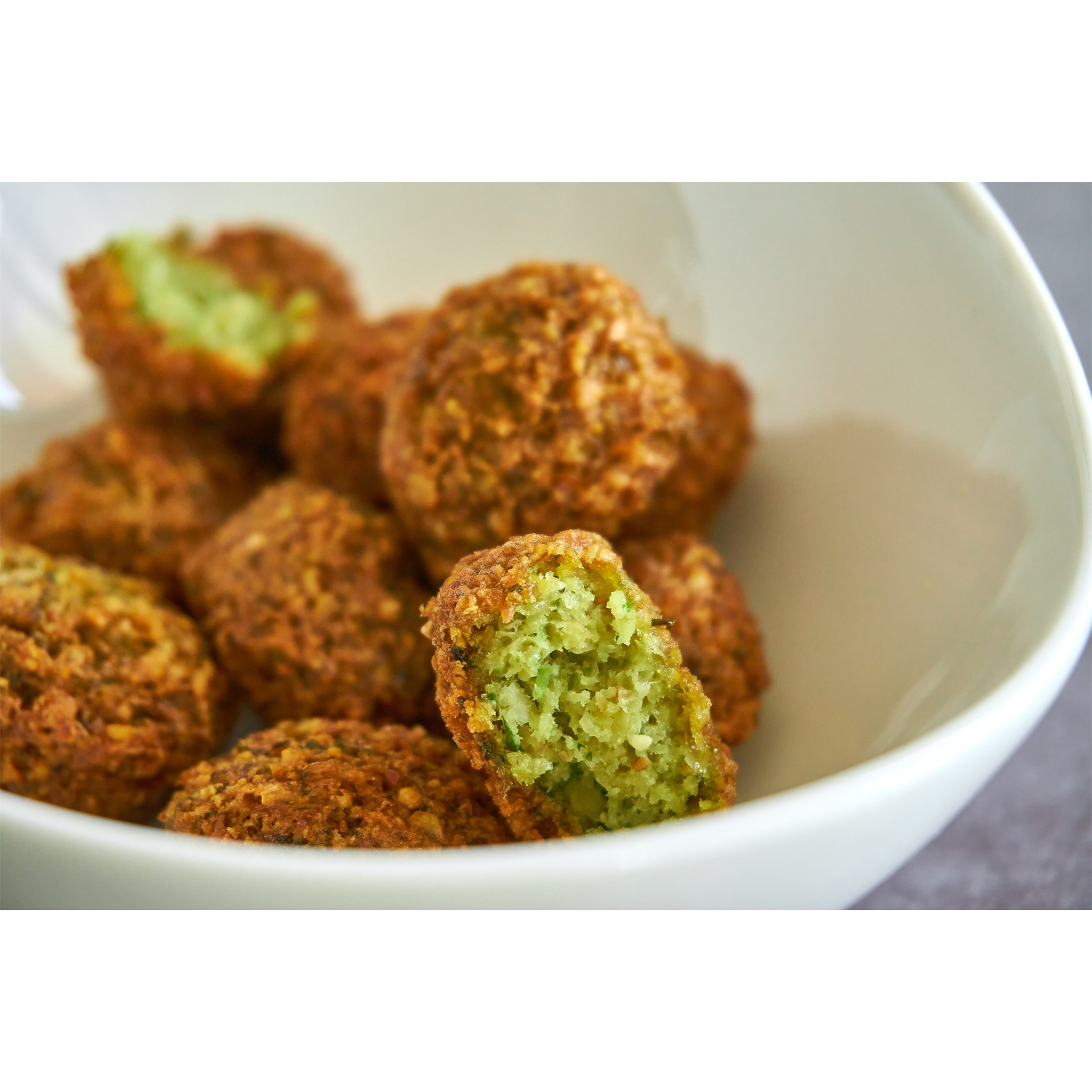 Un bol blanc rempli de boules de falafel frites, dont une est cassée.
