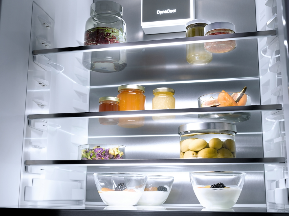 Ein offener Kühlschrank mit Gläsern und Schalen voller Lebensmittel auf Glasböden.