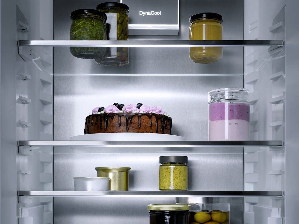 Kühlschrank mit Lebensmitteln: Kuchen, Gläser mit Aufstrichen und Joghurt.