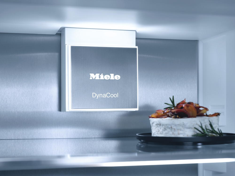 Kühlschrankinneres mit Miele DynaCool-Schild und Käse auf schwarzer Platte.