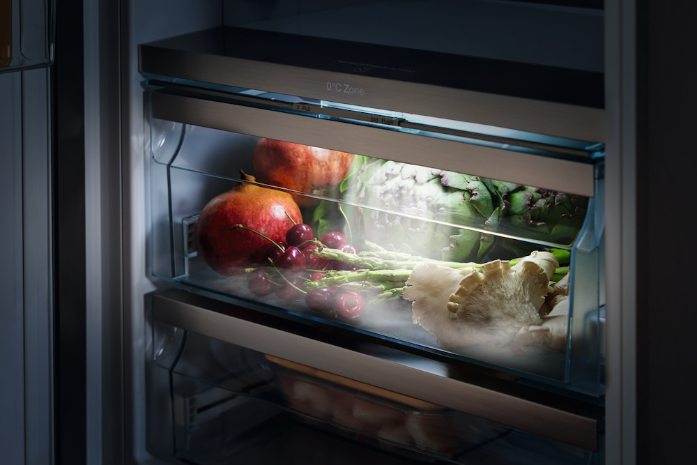 Frische Lebensmittel in einem Kühlschubfach mit Beleuchtung: Granatäpfel, Kirschen, Spargel, Artischocken und Pilze.