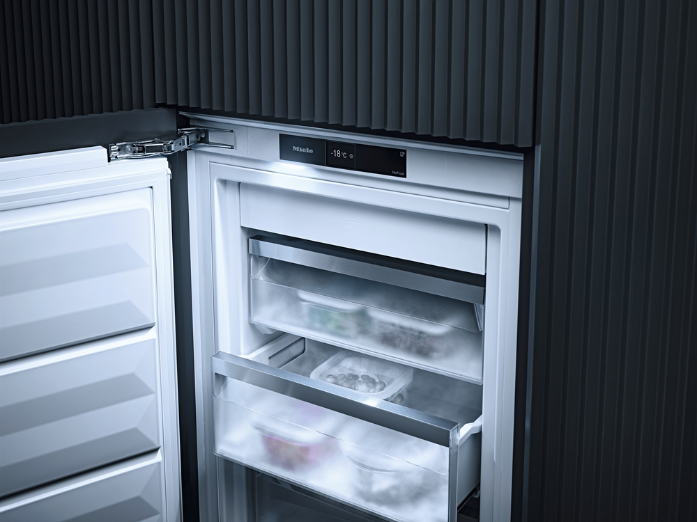 Ein Miele Kühlschrank mit offen stehender Tür, zeigt gefrorene Lebensmittel in Schubladen.