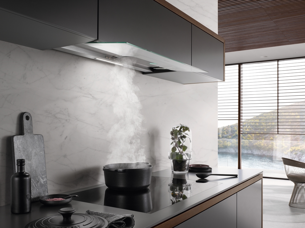 Eine moderne Küche mit schwarzem Topf auf Induktionsherd, Dampf steigt auf. Marmor-Backsplash.
