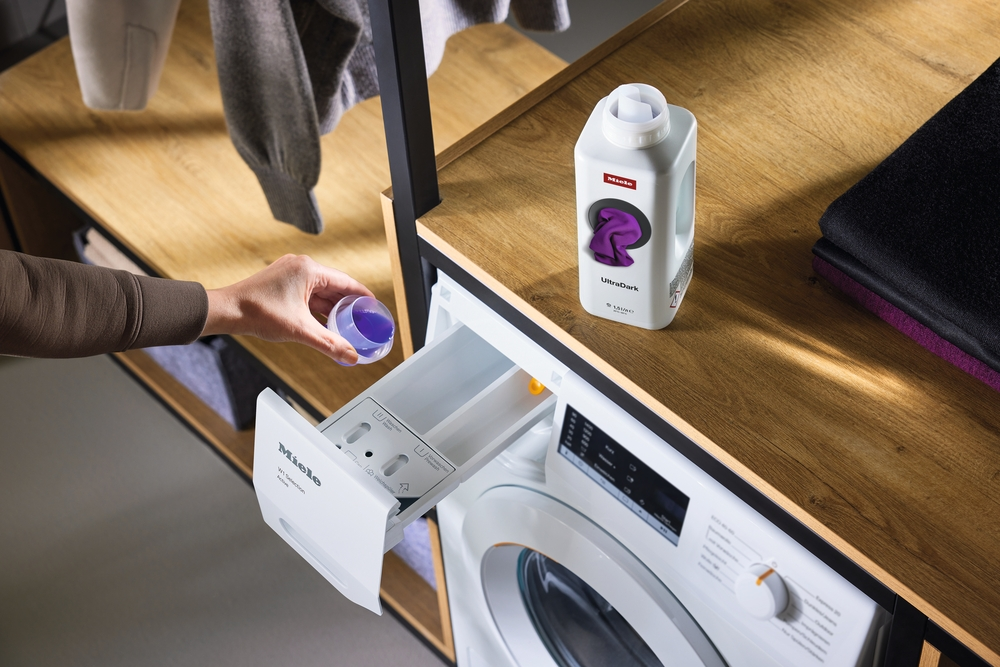 Eine Hand gießt lila Waschmittel in eine Waschmaschine.