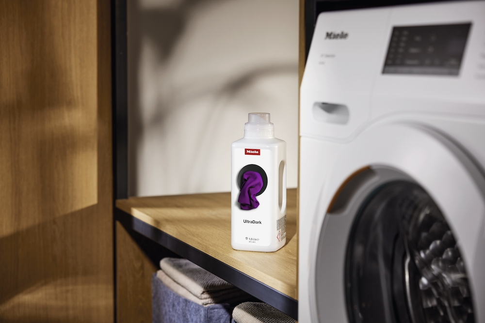 Miele UltraDark Waschmittel neben einer weißen Miele Waschmaschine.