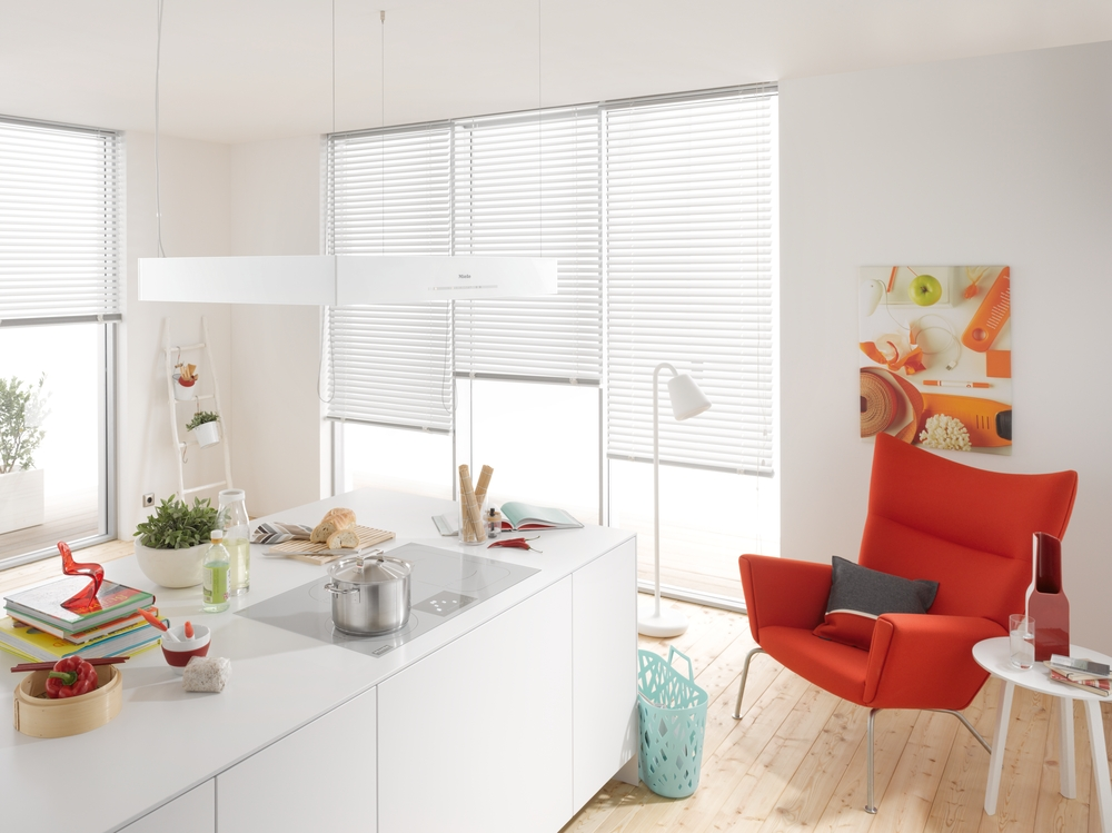 Moderne weiße Küche mit Essbereich, rotem Sessel und Kunstwerk an der Wand.