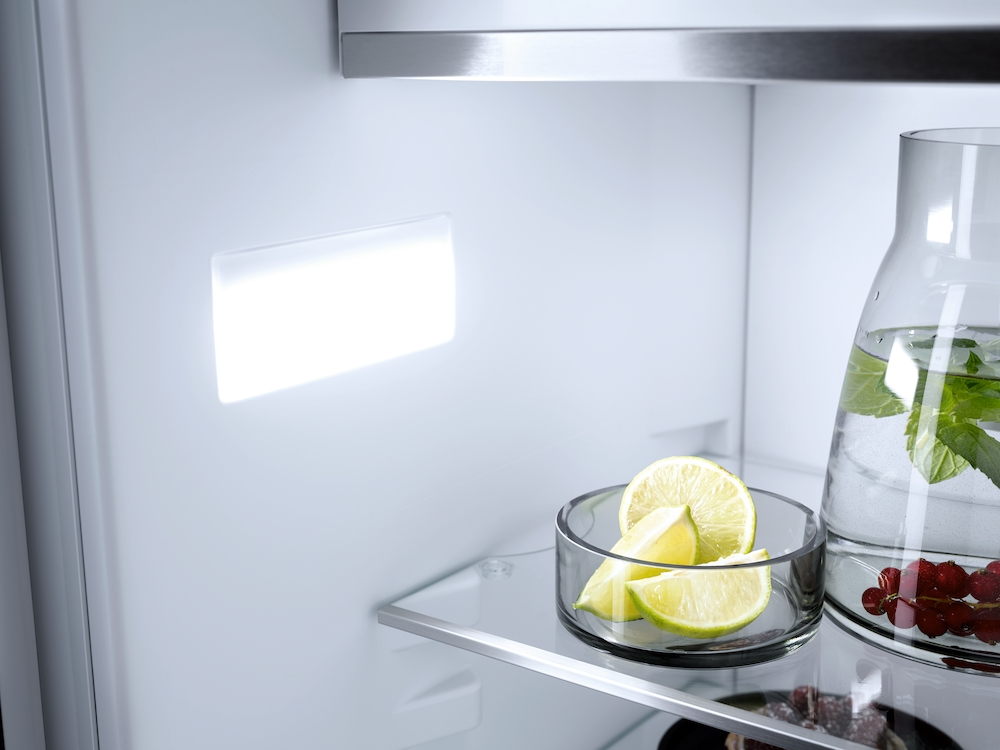 In einem Kühlschrankregal liegen Limettenspalten in einer Schale und ein Krug mit Wasser und Minze.