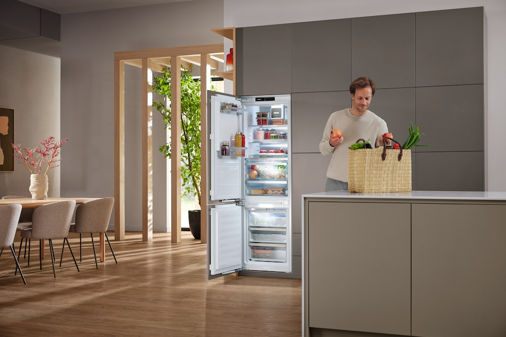 Ein Mann stellt Lebensmittel in einen offenen Kühlschrank in einer modernen Küche.