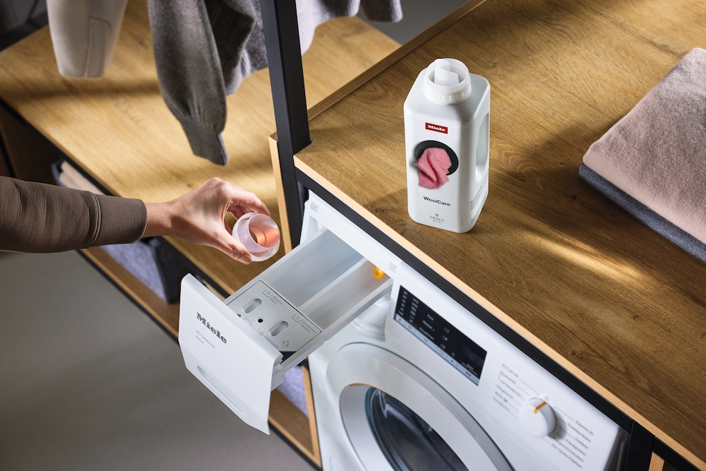 Eine Hand gibt eine kleine Kappe in die Waschmittelkammer einer Miele-Waschmaschine.