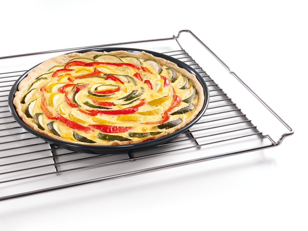 Ein runder Gemüsekuchen mit Zucchini, Paprika und einer hellen Füllung auf einem Gitter.