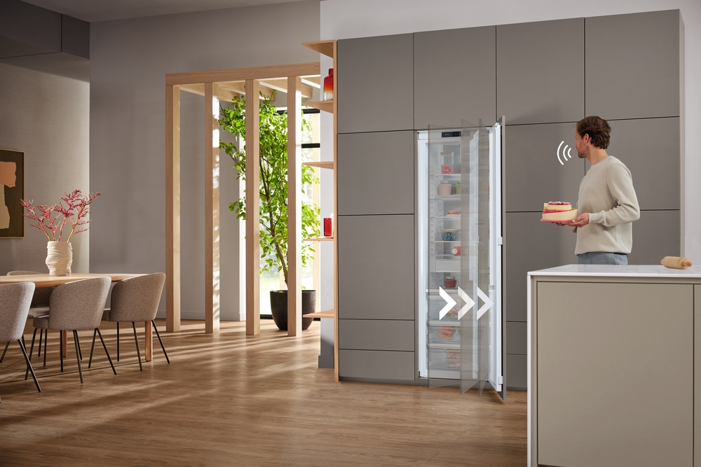 Mann hält Kuchen vor offenem Kühlschrank in moderner Küche mit Essbereich.
