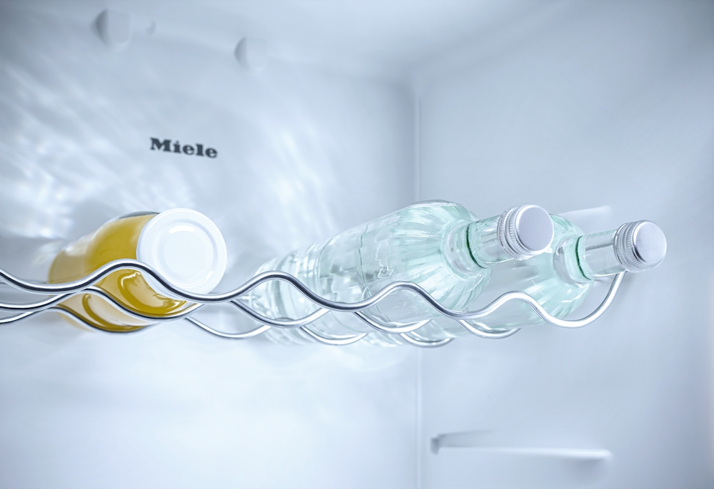 Ein Glas Wein und zwei Flaschen Wasser liegen in einem Miele Kühlschrank.
