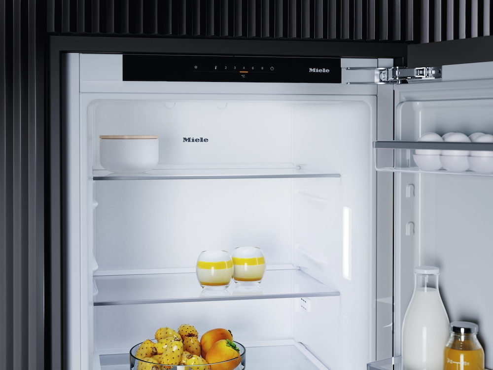 Ein offener Miele-Kühlschrank mit Lebensmitteln, darunter Obst, Eier und Getränke.