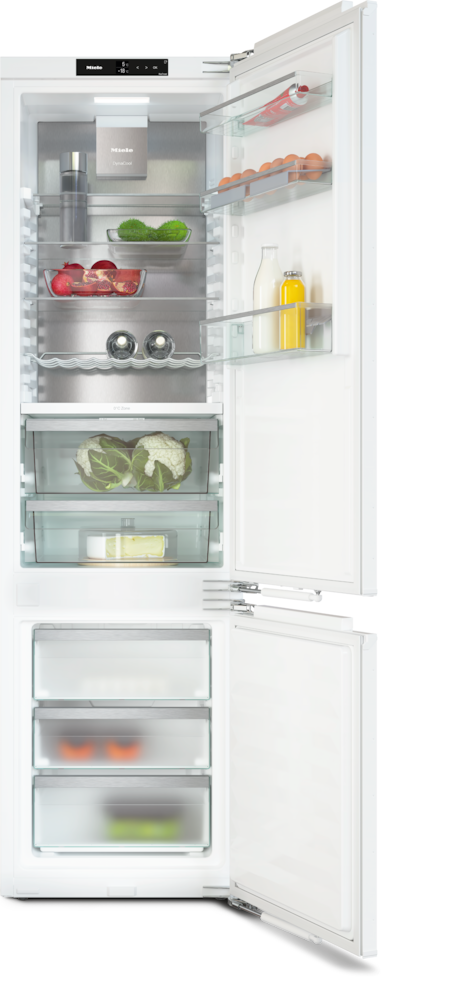 Ein offener weißer Kühlschrank mit Lebensmitteln wie Gurken, Granatäpfeln und Blumenkohl.
