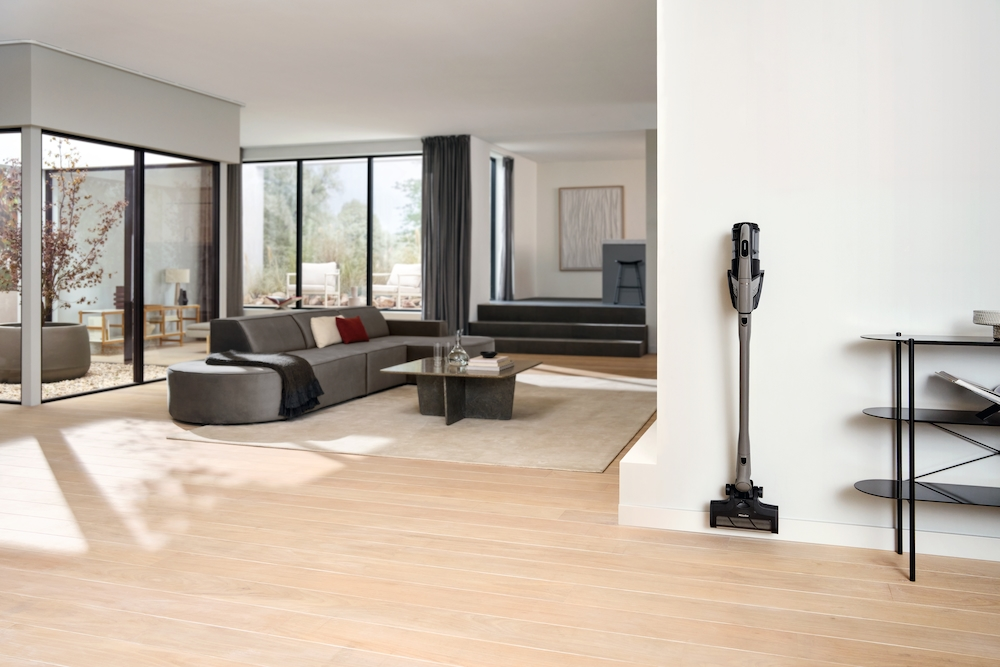Ein moderner Wohnraum mit Sofa, Couchtisch, Staubsauger und großen Fenstern.