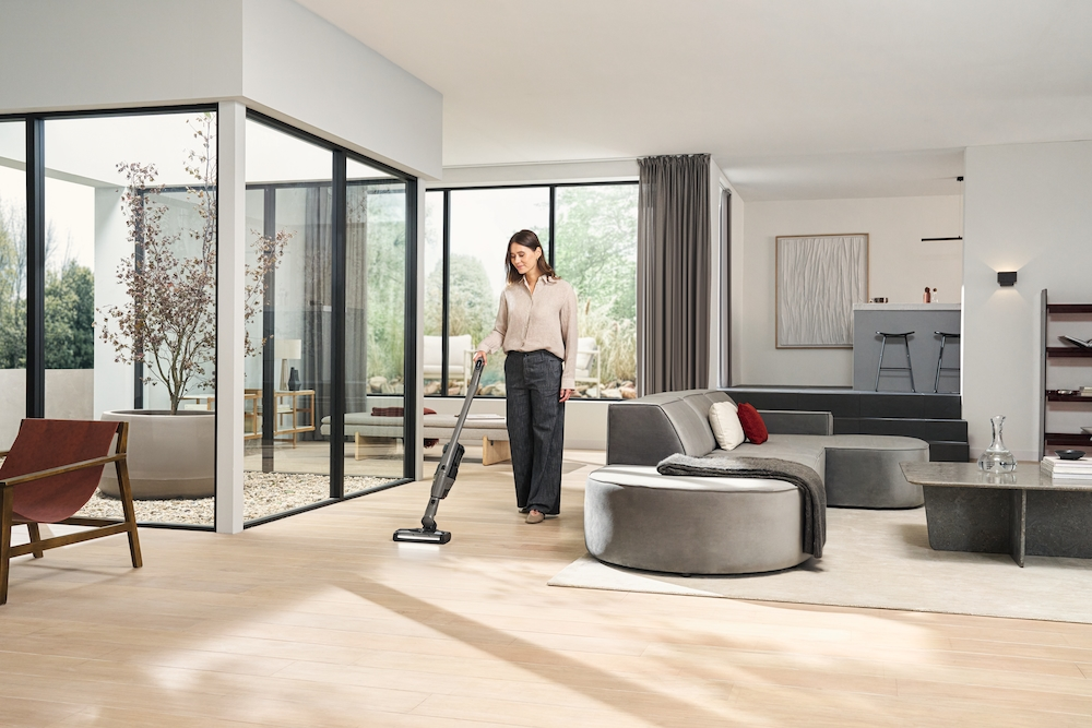 Eine Frau saugt einen modernen Wohnraum mit großen Fenstern, einem Sofa und Möbeln.