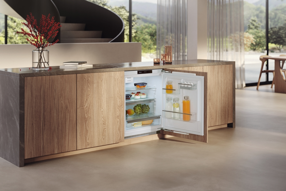 Ein Kühlschrank mit offener Tür in einer modernen Küche mit Holzschränken und einer Wendeltreppe.