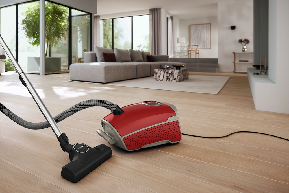 Ein roter Staubsauger auf einem Holzboden in einem modernen Wohnzimmer mit Sofa.