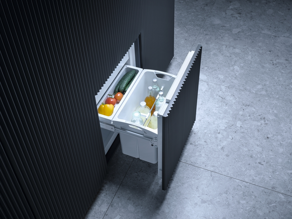 Ein ausziehbarer Kühlschrank mit Gemüse und Flaschen auf grauem Boden.