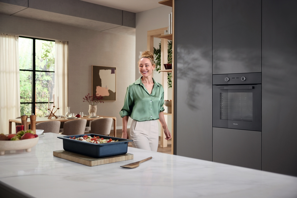 Eine Frau in einem grünen Hemd steht in einer modernen Küche neben einem Backofen.