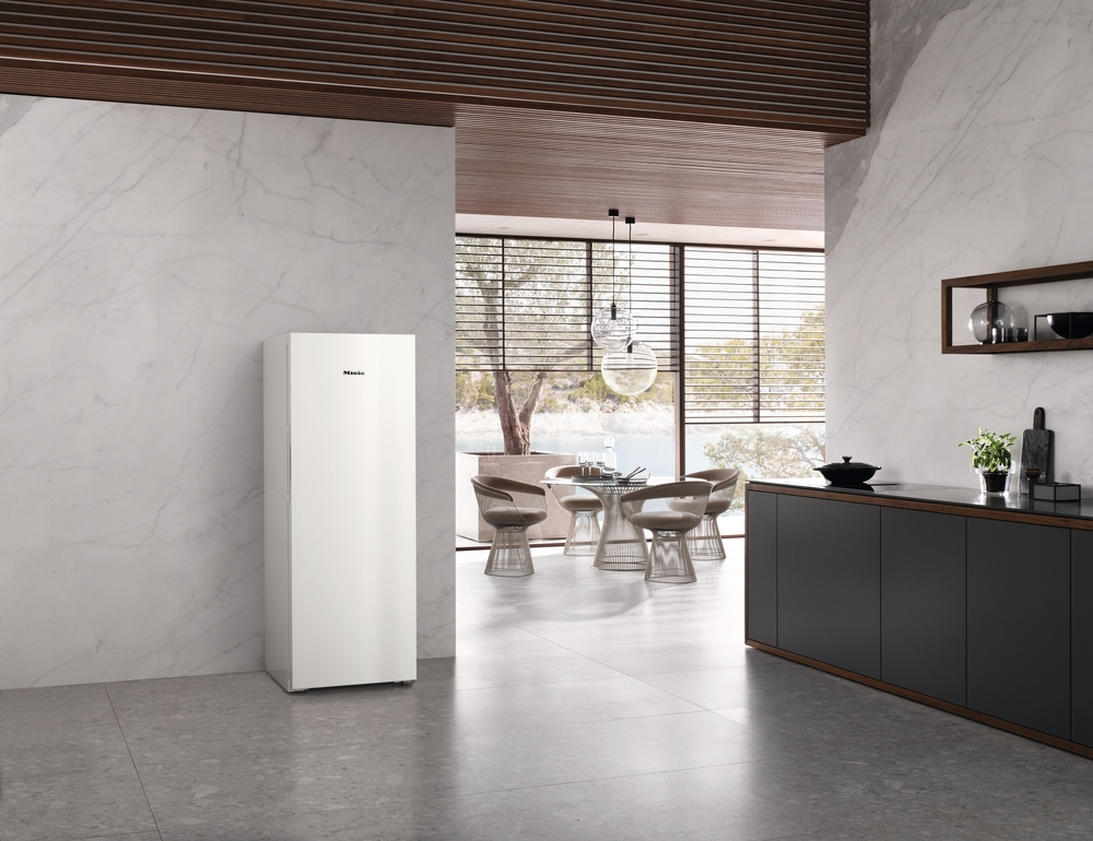 Ein hoher weißer Kühlschrank steht in einer modernen Küche mit Marmorwänden und Essbereich.