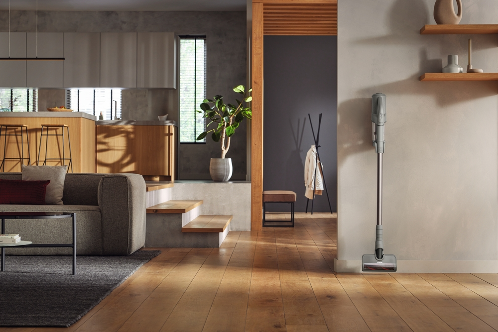 Ein moderner Wohnbereich mit Sofa, Küchentheke, Staubsauger und Holzboden.