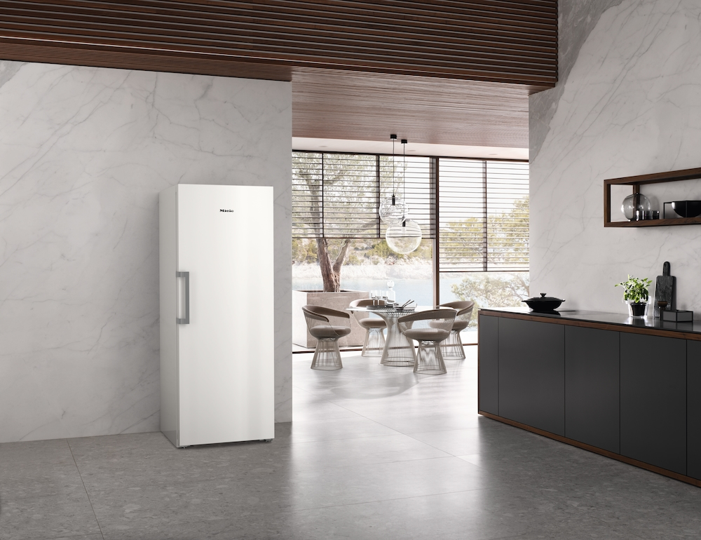 Ein moderner weißer Kühlschrank steht in einer Küche mit Marmorwänden und Blick auf einen Essbereich.