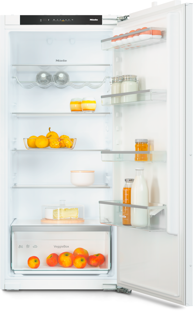 Ein offener Kühlschrank mit Lebensmitteln: Eier, Gläser, Obst, Käse und Äpfel in der Gemüseschublade.