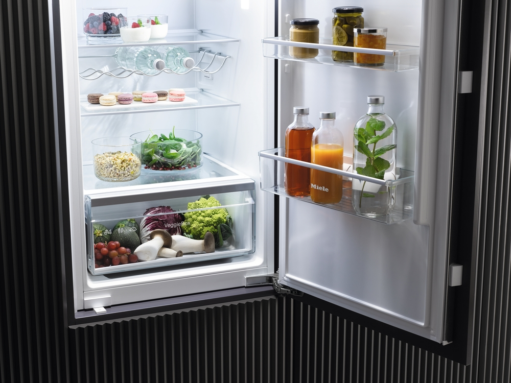 Offener Kühlschrank mit Lebensmitteln: Beeren, Joghurt, Wasser, Makronen, Salat, Gemüse und Getränke.