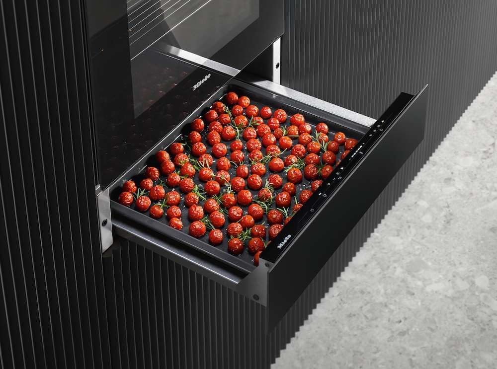 Ein offenes Schubfach mit vielen Kirschtomaten auf einem schwarzen Blech.