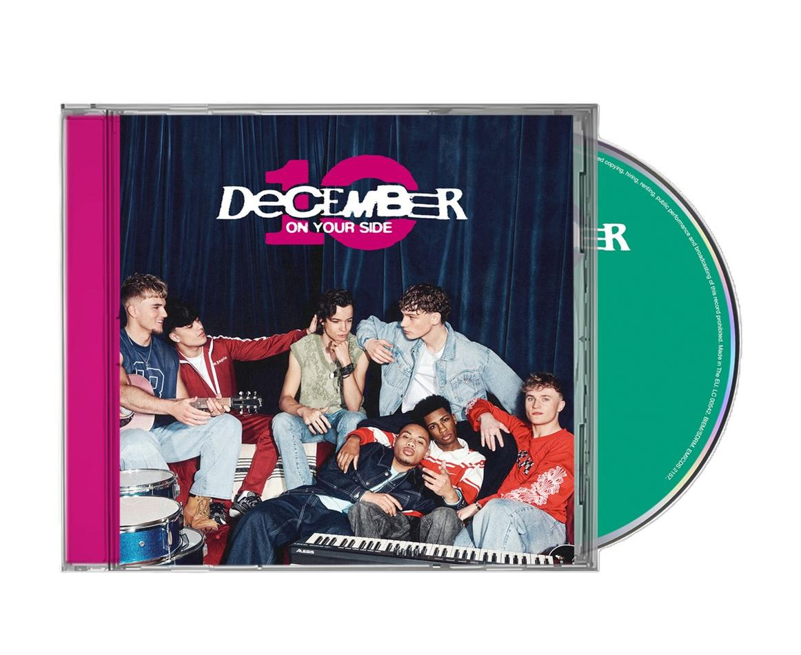 Sieben junge Männer posieren vor einem blauen Vorhang mit der Aufschrift „December On Your Side“.