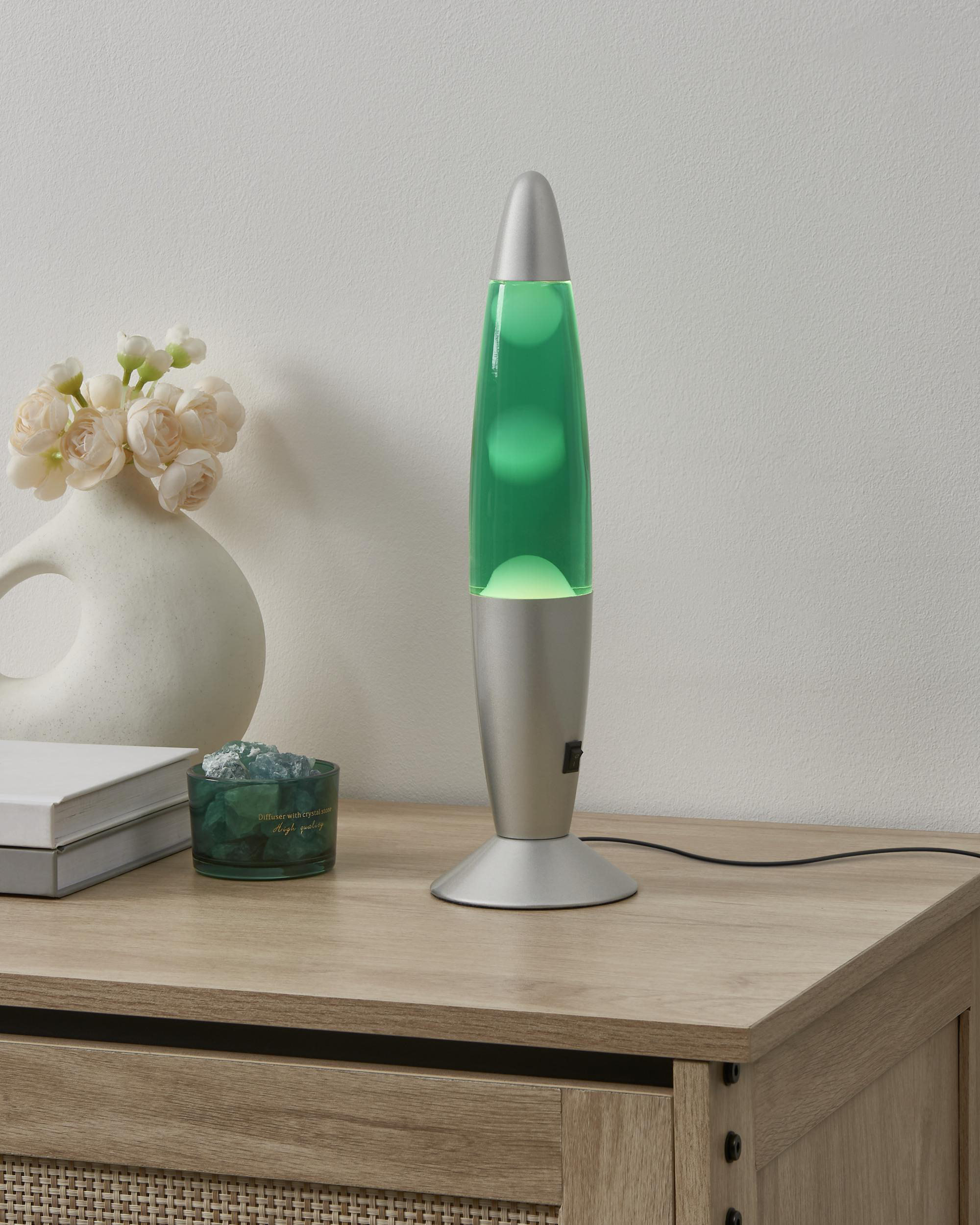 Eine grüne Lava-Lampe leuchtet auf einem Holztisch neben Blumen und Büchern.