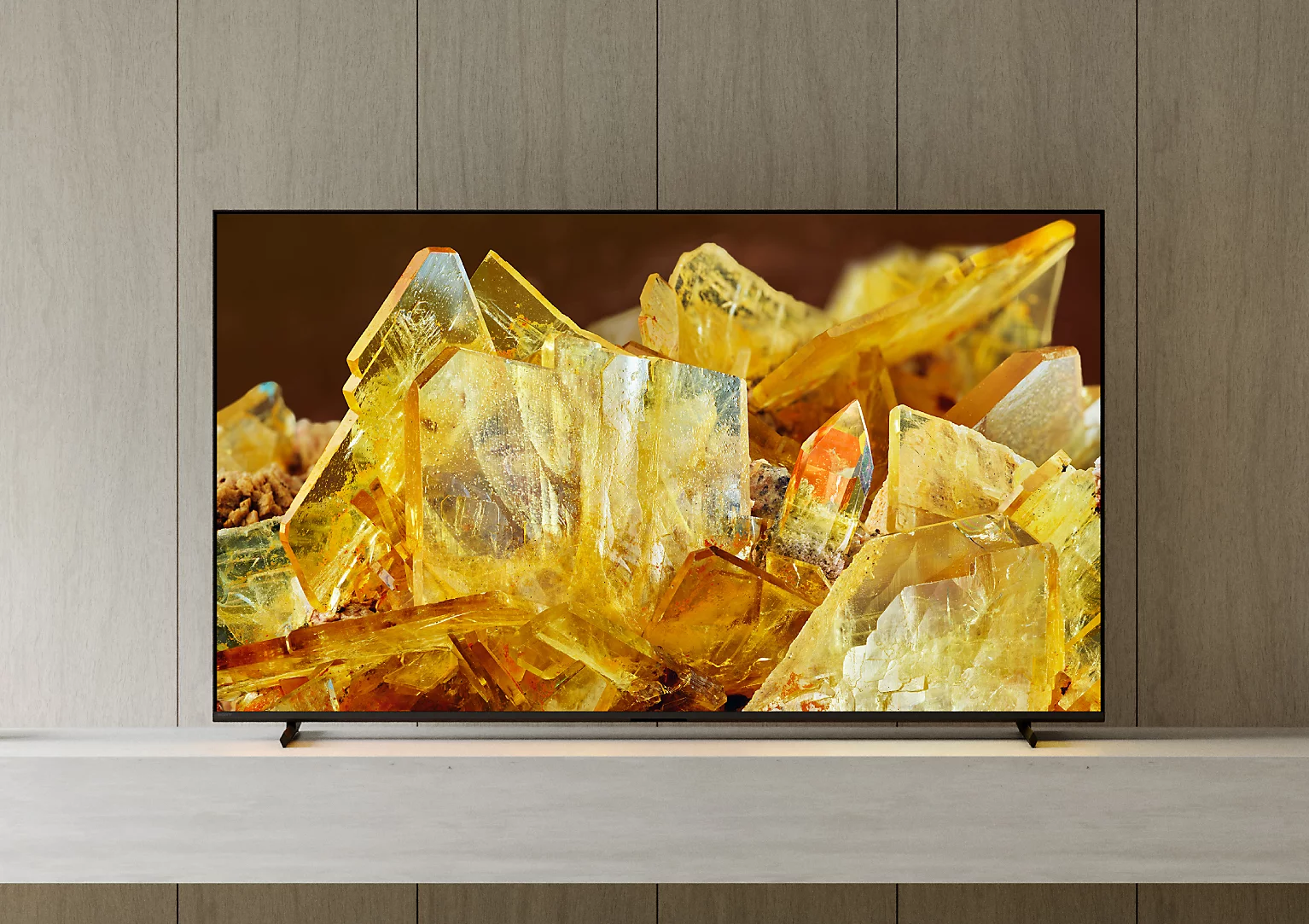 Egy TV képernyő sárga kristályokat jelenít meg fa háttér előtt.