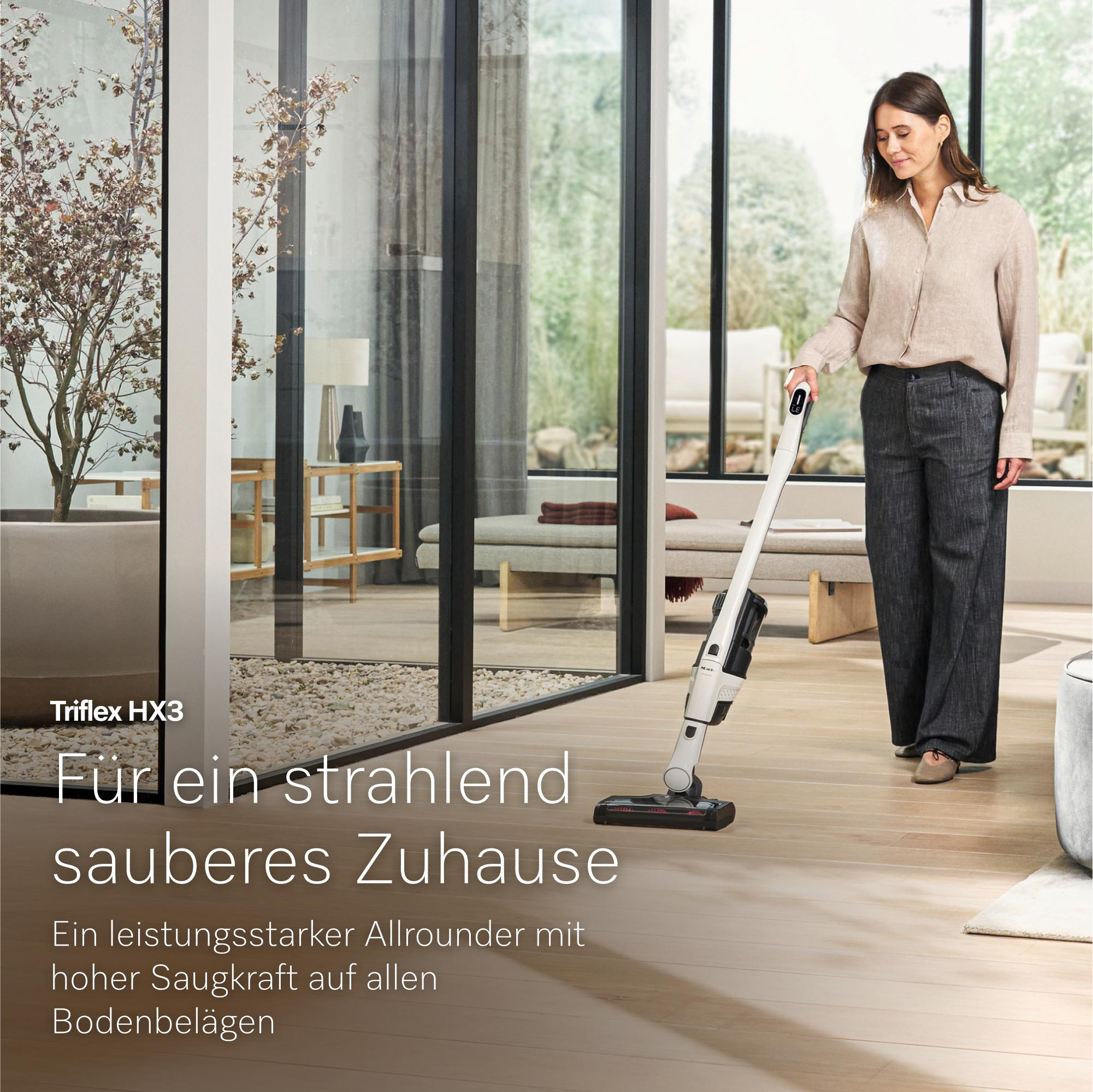 Eine Frau saugt mit einem Triflex HX3 Staubsauger einen Holzboden in einem modernen Zuhause.