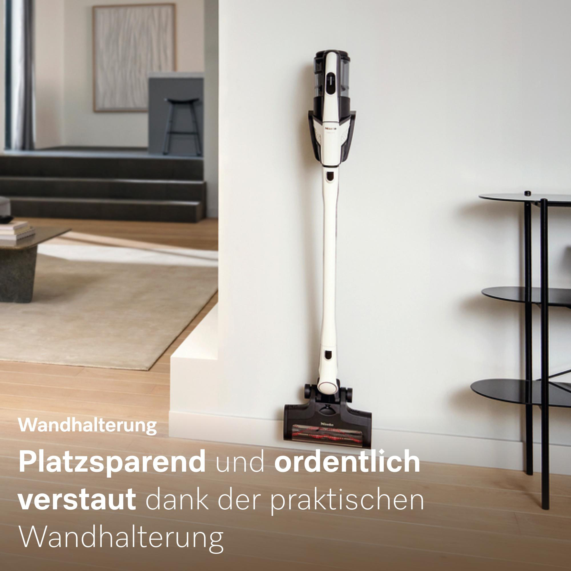 Ein weiß-schwarzer Staubsauger hängt an einer Wandhalterung neben einem Regal.