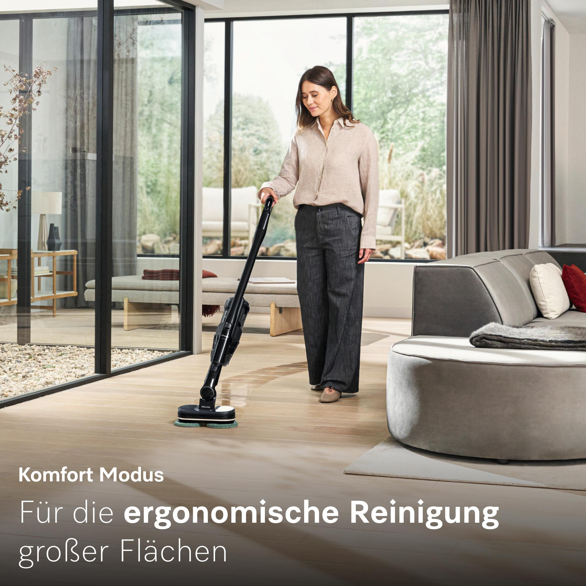 Frau reinigt den Boden mit einem kabellosen Staubsauger in einem modernen Wohnzimmer.
