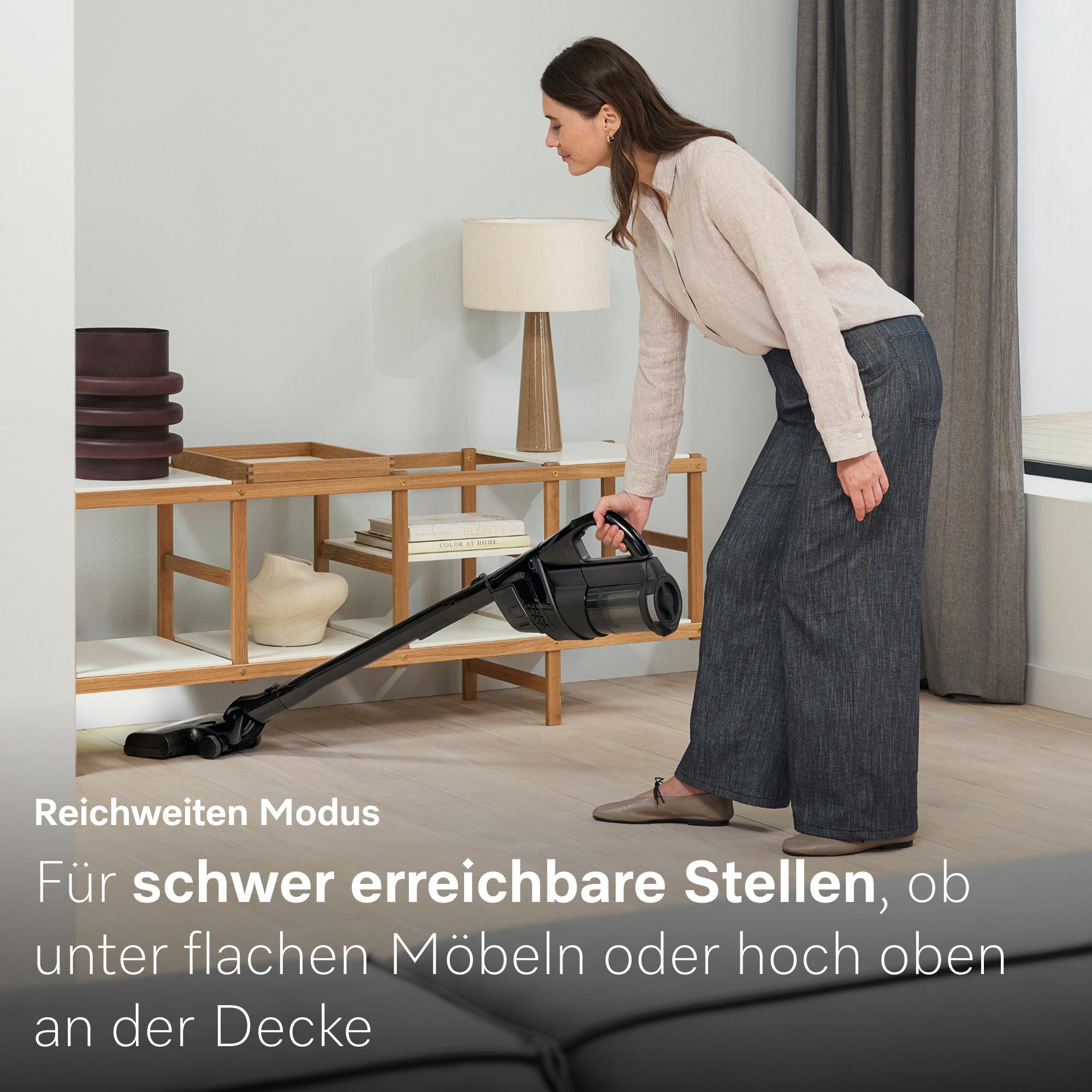 Eine Frau saugt den Boden unter Möbeln mit einem Handstaubsauger.