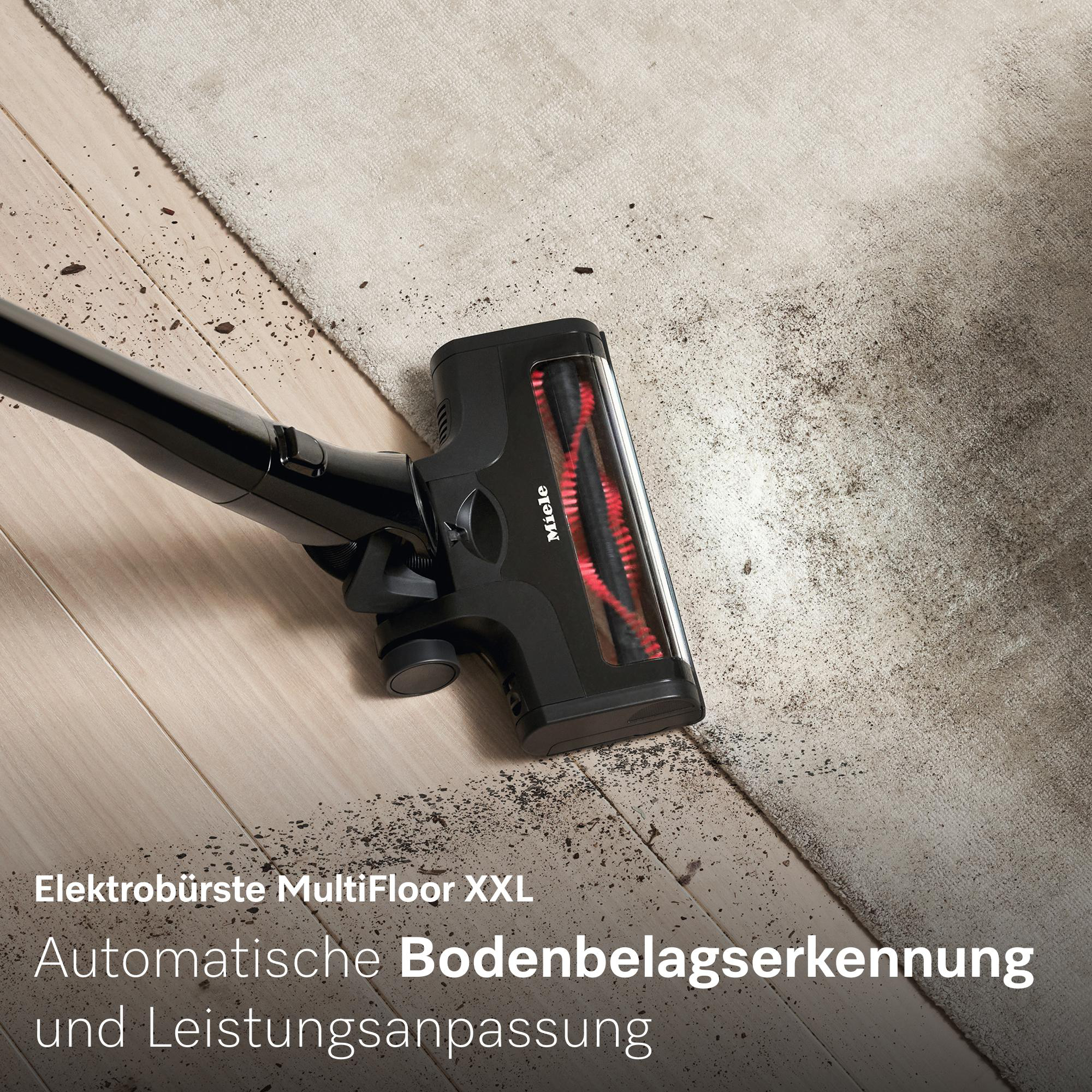 Schwarzer Staubsaugerkopf auf Holz und Teppich mit Schmutzpartikeln.