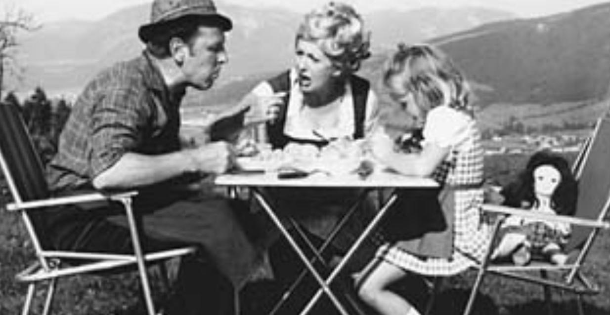 Familie isst im Freien, Mann mit Hut, Frau und Kind am Tisch.