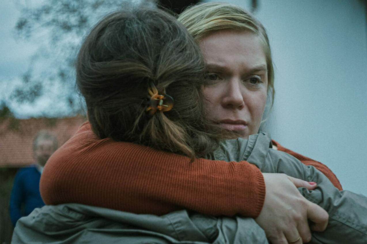 Zwei Frauen umarmen sich. Eine trägt einen orangefarbenen Pullover.