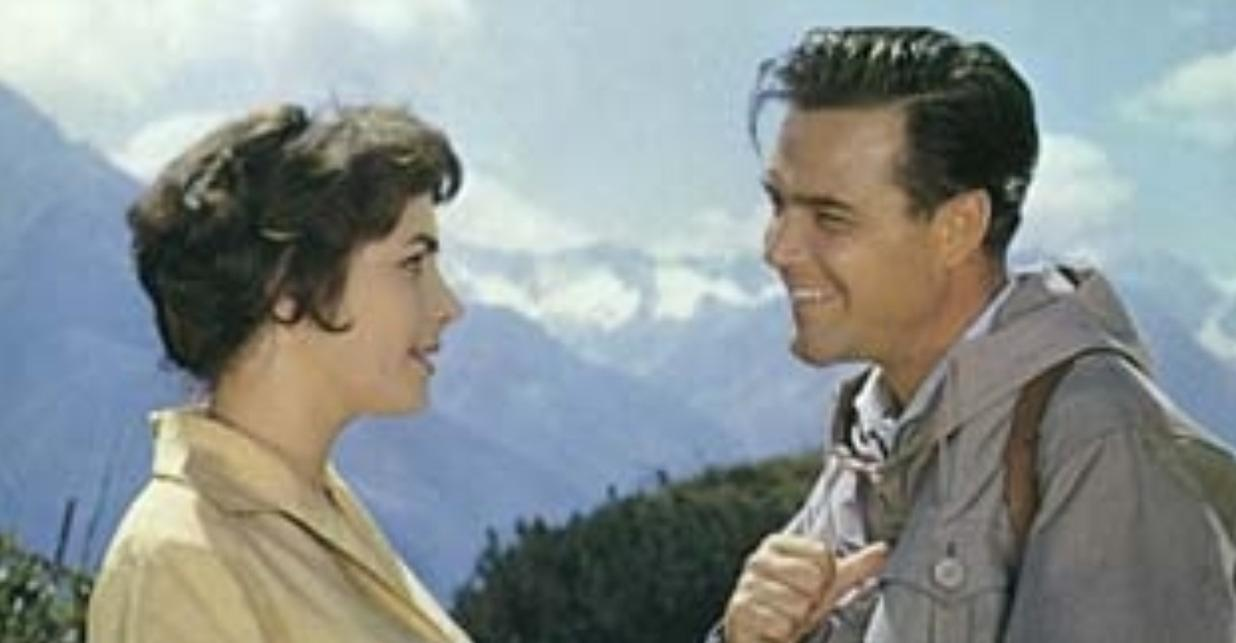 Mann und Frau lächeln sich an vor Bergkulisse.
