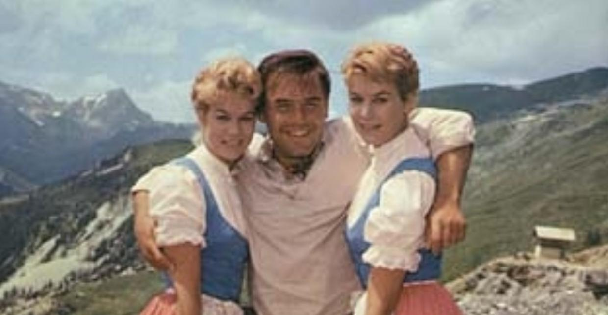 Ein Mann mit zwei Frauen in Tracht vor Bergkulisse.