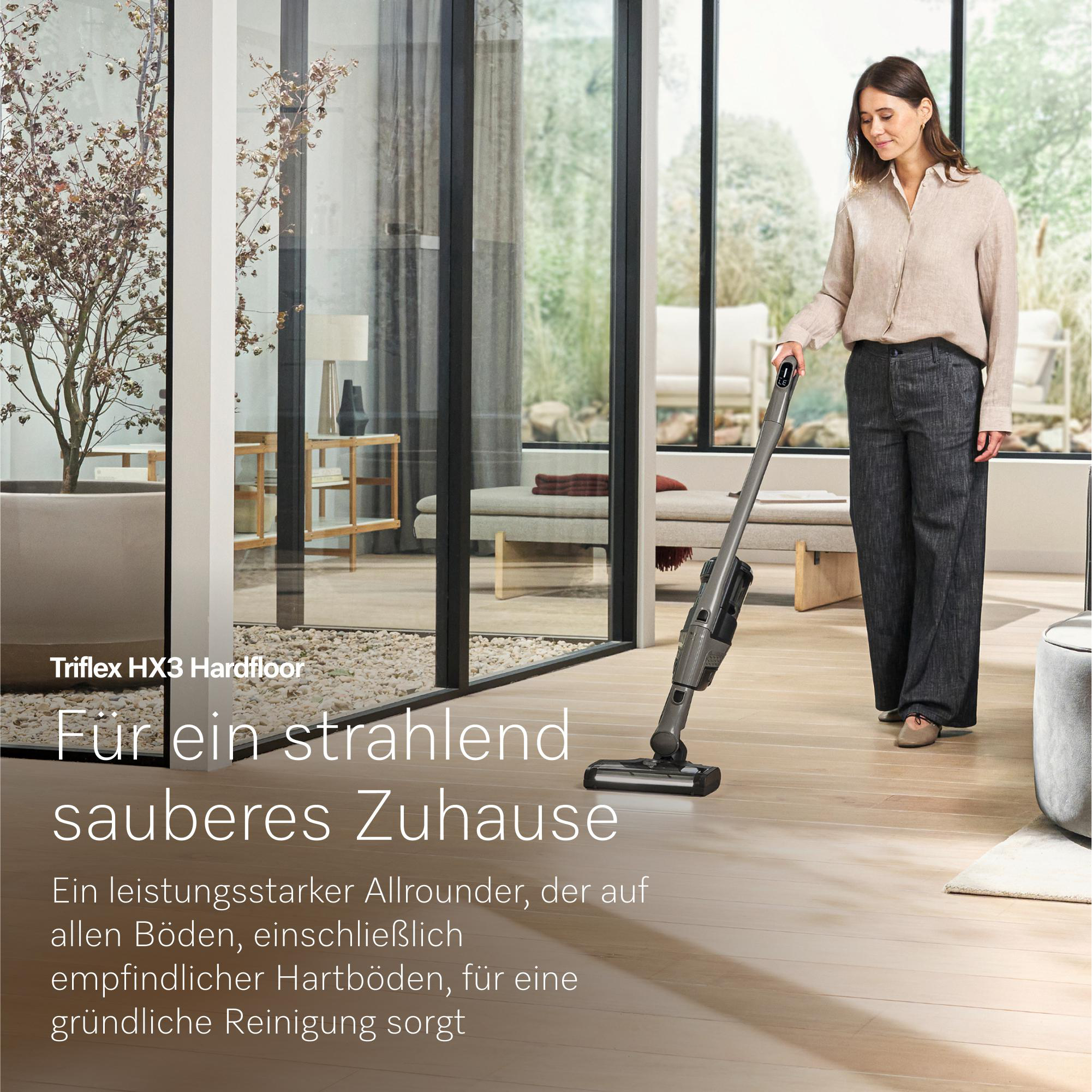Eine Frau saugt mit einem Handstaubsauger einen Holzboden in einem modernen Wohnzimmer.